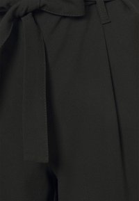 Zwarte stoffen broek met een gladde textuur, voorzien van een gestrikt middenstuk en geplooid voorpand.