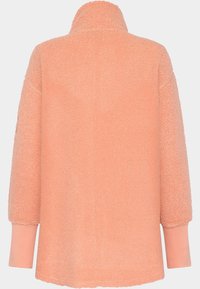 Persikofärgad fleecejacka med hög krage, långa ärmar och textilstruktur. Sömlös design med ribbade manschetter och avslappnad passform.