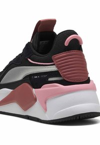 Zapatilla textil negra con acentos de ante, raya metálica plateada, detalles en goma rosa y media suela blanca. Presenta una pestaña en el talón texturizada.