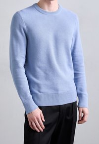Light blue knitted sweater with a textured pattern, round neckline, ribbed cuffs and hem, paired with black trousers.