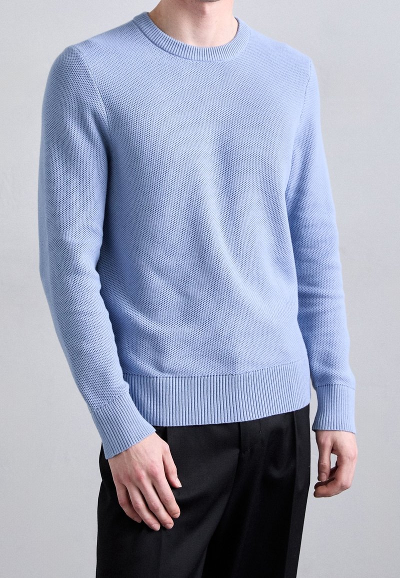 Light blue knitted sweater with a textured pattern, round neckline, ribbed cuffs and hem, paired with black trousers.