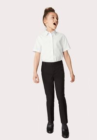 White short-sleeve button-up shirt paired with black tailored pants and black slip-on shoes. Smooth fabric, fitted design, minimal detailing.