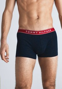 Marineblaue Boxershorts aus weichem Stoff, mit einem roten Bund, der das Logo "TOMMY HILFIGER" trägt. Eng anliegendes Design.