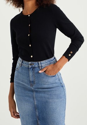 Cardigan noir avec des boutons dorés, manches ajustées et texture côtelée, associé à une jupe en denim bleu clair, à taille haute et avec poches avant.