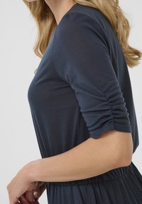 Robe bleu marine avec des manches longues froncées, un corsage ajusté et une jupe évasée. Fabriquée dans un tissu doux et léger avec une texture lisse.