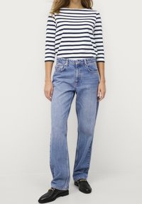 Gestreepte marineblauwe en witte langeblauw T-shirt gecombineerd met lichtblauwe wijde broek. De broek heeft vijf zakken en een ontspannen pasvorm. Zwarte loafers zijn inbegrepen.