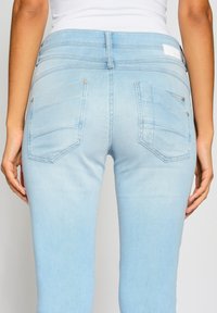 Světle modré džíny z denimu s hladkou strukturou, obsahující dvě zadní kapsy a jemné detaily šití. Střední výška pasu.