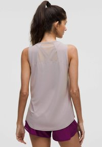 Haut de sport sans manches beige clair avec un panneau en maille à l'arrière, associé à un short violet foncé. Texture lisse, coupe ajustée.