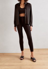 Svart knappad skjorta över en svart crop top och tighta leggings. Släta svarta öppna tofflor. Slätt tyg, minimalistisch design, skräddarsydd passform.