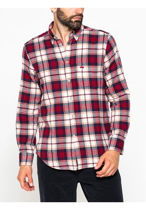 Uomo che indossa una camicia a quadri rossa, blu navy e bianca con bottoni e maniche lunghe e pantaloni neri, ritagliata sotto il mento e a metà coscia.