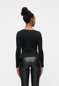 Μαύρο τοπ μακρυμάνικο με στρογγυλή λαιμόκοψη, εφαρμοστή γραμμή και απαλό υλικό, σε συνδυασμό με μαύρο κολάν, αναδεικνύοντας μια κομψή σιλουέτα.