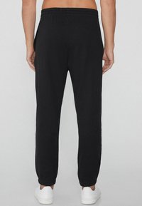 Pantalones jogger negros de tela suave, con cinturilla elástica, bolsillos laterales y puños en los tobillos. Diseño simple y aerodinámico.