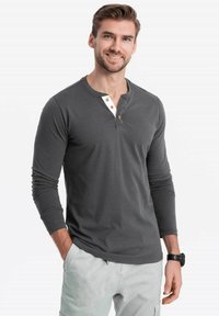Graues Langarmhemd mit Henley-Kragen, mit einer weißen Knopfleiste und Holzknöpfen. Weicher Stoff, taillierte Form.