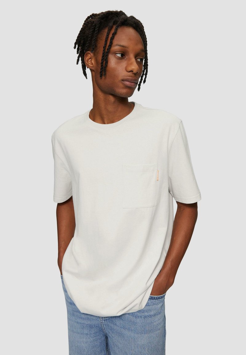 Lichtgrijs katoenen t-shirt met korte mouwen, ronde hals en een borstzak; voorzien van een klein oranje label nabij de zak.