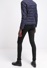 Marin puffjacka med horisontell quiltning, rund halsringning och långa ärmar, tillsammans med svarta skinny jeans och ankelstövlar.