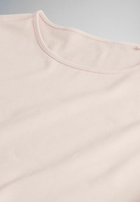 Camiseta de color rosa claro con cuello redondo que muestra una textura de tela suave y costuras finas a lo largo del borde del cuello.