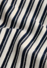 Tissu blanc avec des rayures verticales bleu marine espacées régulièrement, montrant un motif tricoté texturé et de légers plis dans le tissu.