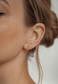 Goldene Ohrmanschette mit drei kleinen Edelsteinen, die ein gebogenes Design aufweist und sich eng an das Ohr anschmiegt. Glatte Metalloberfläche mit polierter Oberfläche.