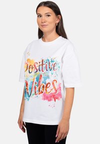 Witte T-shirt met kleurrijke aquarelstijl tekst "Positive Vibes", met korte mouwen en een ontspannen pasvorm.