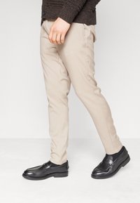 Beige skräddarsydda byxor i kombination med svarta läderloafers. Outfiten har en åtsittande passform och en mjuk textur som fångar en modern och avslappnad stil.