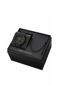 Svart analog klocka med mesharmband, som har en rund urtavla, guldaccenter och tre sub-dialer, presenterad i en svart låda märkta "Armani Exchange."