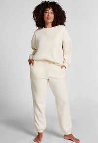 Loungewear-set in roomkleur, bestaande uit een losvallend sweatshirt met een ronde hals en een broek met trekkoord en zijzakken. Zachte textuur.
