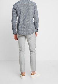 Långärmad skjorta med marinblå bas och små vita blommönster, kombinerat med ljusgrå smalpassande byxor och vita sneakers.