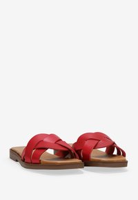 Sandalias deslizantes de cuero rojo con tiras trenzadas, suela plana y base marrón. Presentan una textura suave y un diseño minimalista.