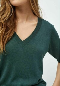 Top verde de manga corta con cuello en V, fabricado en un tejido brillante con una textura suave y detalles de canalé en el escote.