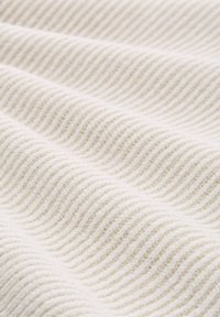 Cremfarbener Stoff mit einer gerippten Textur, der wellenartige Muster zeigt, die Tiefe und eine taktile Qualität schaffen. Weich und leicht.