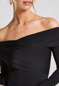 Μαύρη εκτός ώμου μπλούζα με μακριά μανίκια, που διαθέτειGathered fabric και λεία υφή. Τακτοποιημένη τελειώση γύρω από την κοπή του λαιμού.