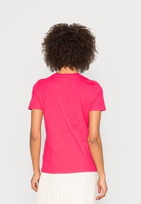 T-shirt aderente a maniche corte in cotone rosa brillante, con un semplice scollo rotondo e una texture liscia. Vista posteriore mostrata.