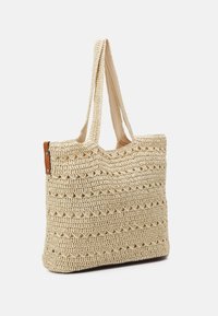 Geweven boodschappentas in crèmekleur, met een geprofileerd patroon en twee stoffen handvatten. Aan één kant afgewerkt met bruin leer.