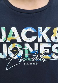 Tricou din bumbac bleumarin, cu text imprimat vibrant "JACK & JONES Essentials" și modele colorate de stropi, cu guler curbat.