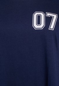 Tamsiai mėlynas medvilninis marškinėliai, su baltu skaičiumi „07“ ryškiu, kontūruotu šriftu kairėje pusėje. Audinys turi lygų paviršių.