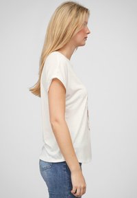 T-shirt en coton blanc à manches courtes avec un col rond, arborant un motif sur le devant. Associé à un jean en denim bleu.