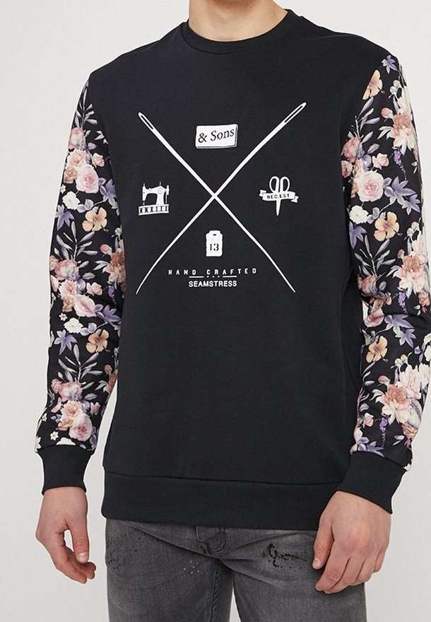 Sweat noir avec manches à motif floral et graphiques blanches sur le thème de la couture ainsi que du texte sur la poitrine, comprenant des aiguilles, des ciseaux et une machine à coudre.