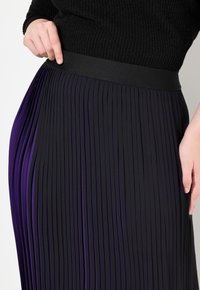 Gonna a pieghe nera con accenti viola, con una cintura liscia e pieghe verticali, che mette in evidenza una combinazione di texture e variazione di colore.