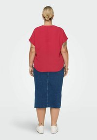 Röd kortärmad topp med rundad nederkant, kombinerad med en denim midi-kjol med en bakre söm och fransad nederkant. Bärs med vita sneakers.