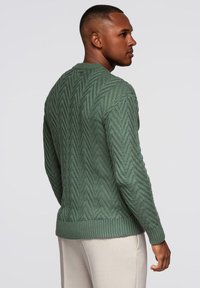 Zielony sweter z dzianiny z wzorem w zygzak, ściągaczami na mankietach i na dole. Projekt ma teksturowane wykończenie oraz krój z okrągłym dekoltem.