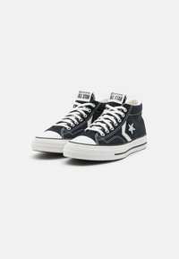 Sneaker alte in tela blu con suole e punte bianche in gomma. Presentano lacci bianchi e un accento a forma di stella sul lato.