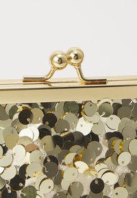 Złote metalowe zapięcie z dwoma okrągłymi gałkami na materiale pokrytym cekinami w odcieniach złota i srebra.