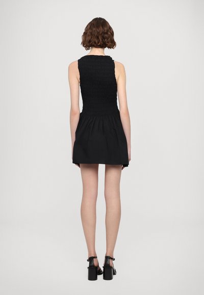 Black dress featuring a smocked bodice, flared skirt, and a textured fabric. Worn with black heeled sandals and a plain background.