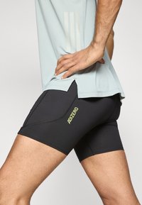 Czarne sportowe spodenki wykonane z elastycznego materiału, z żółtym logo „ADIZERO”, o dopasowanym kroju i ze szwem ozdobnym.