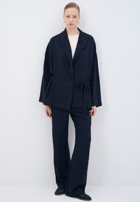 Navy blue kimono-style jacket with a belt, textured fabric, wide sleeves, paired with matching wide-leg trousers and slip-on shoes.