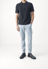 Czarna polo z prążkowanym wzorem i zapięciem na zamek, w połączeniu z jasnoszarymi zwężanymi spodniami i czarnymi botkami. Prosty design, bez widocznych wzorów.
