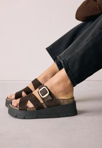 Sandale cu platformă din suede maro, cu curele intersectate, un accent din aur și un mijloc din plută texturată pe o talpă din cauciuc negru.
