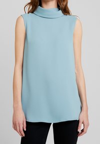 Ljust blå ärmlös topp med hög, veckad halsringning, tillverkad av slätt tyg, med en avslappnad silhuett och rak fåll.