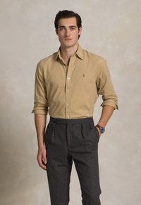 Bežna srajca s dolgimi rokavi, z gumbom, v kombinaciji s sivimi visokimi hlačami. Gladek material, krojen fit, minimalističen dizajn.