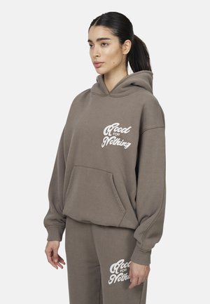 Sweatshirt à capuche marron avec texte blanc, texture douce, poche kangourou et coupe décontractée. Assorti avec un pantalon de jogging présentant le même texte.